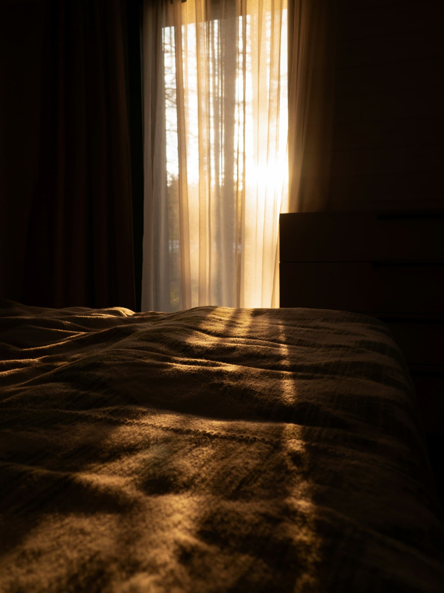 El sol atraviesa una cortina y baña una cama de luz cálida